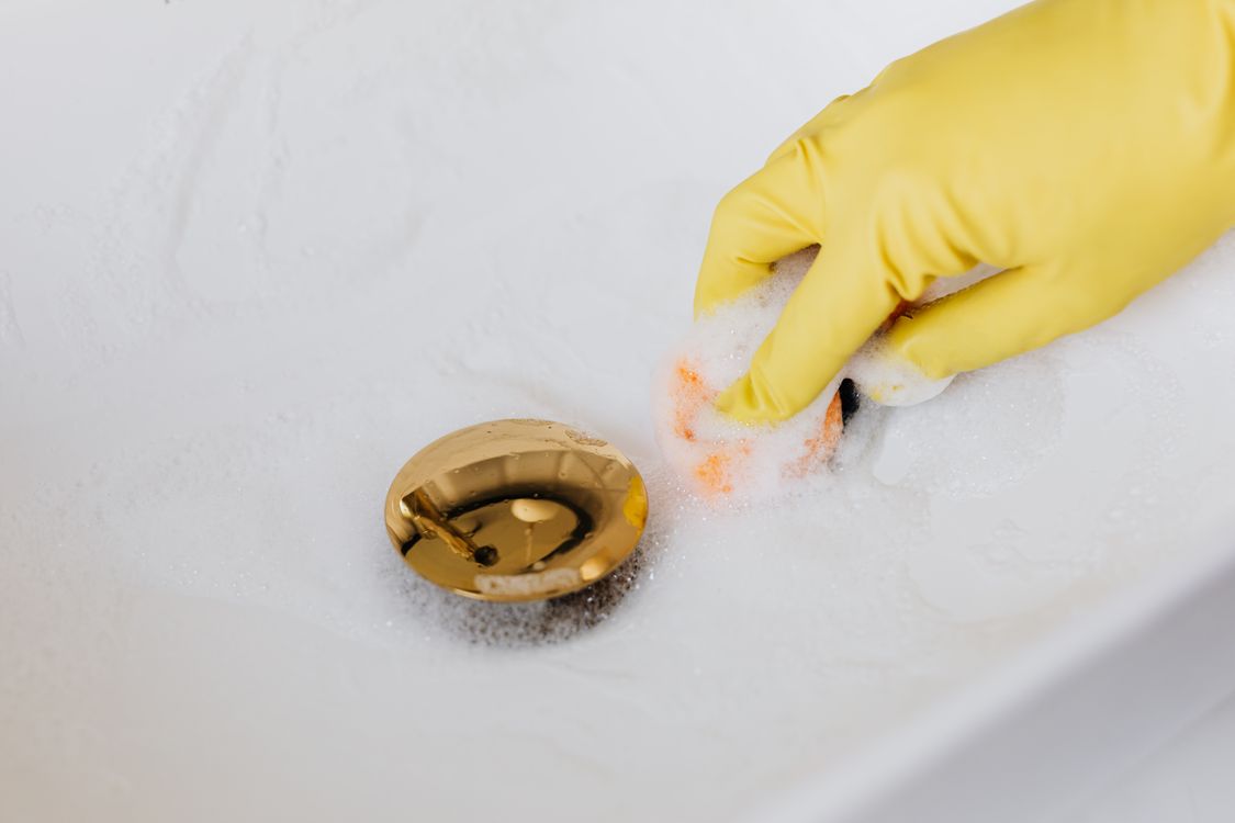 Persoon met gele rubberen handschoenen reinigt de wastafel in de badkamer