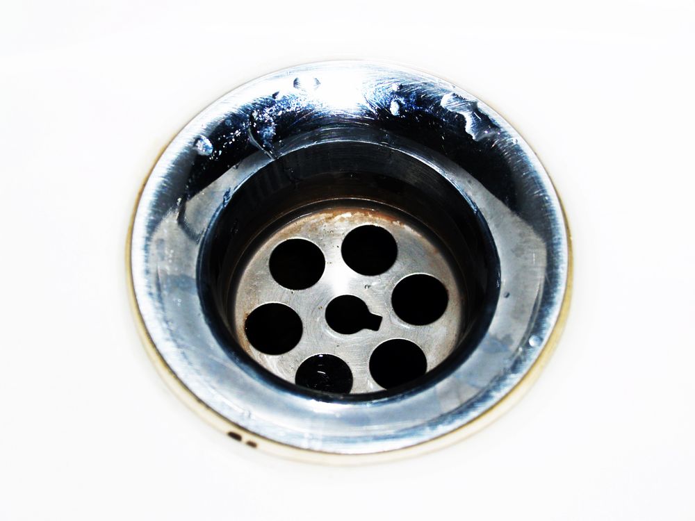 Close-up van een chroom afvoerputje met waterdruppels