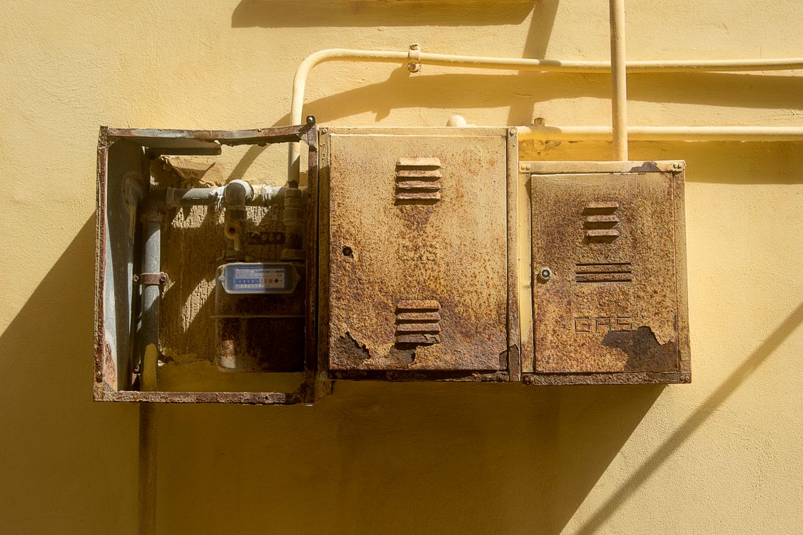 Verouderde leidingen en watermeter tegen een gele muur