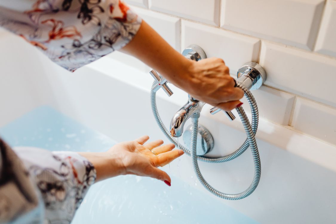Handen die de temperatuur van kraanwater bij de wastafel aanpassen