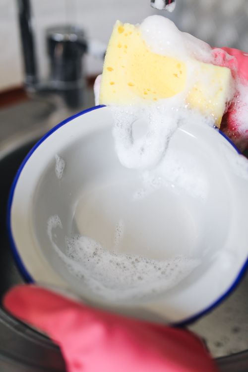 Afwassen van een kom met een gele spons en zeepsop na het koken