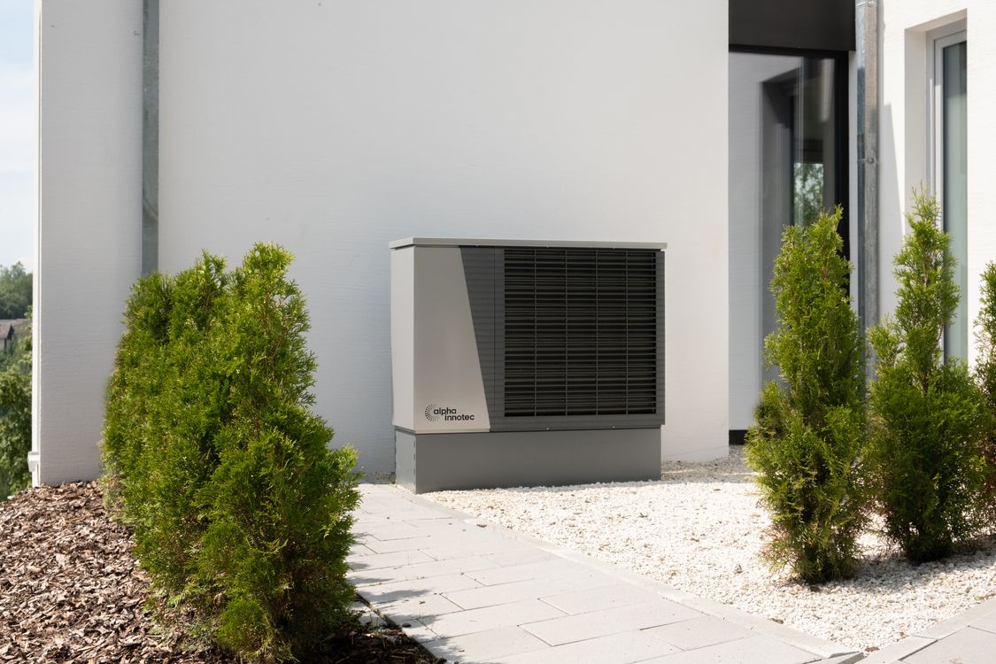 Buitenunit van een warmtepomp gemonteerd aan de gevel van een woning